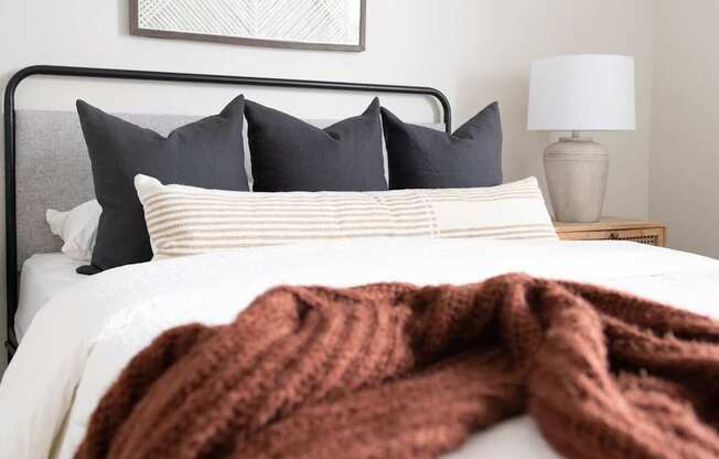 A bed with a white comforter and a brown blanket.