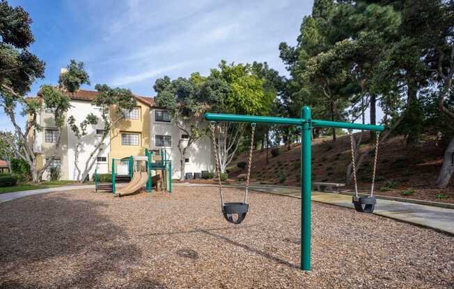 A playground with a green swing set and a building in the background.