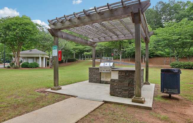 A wooden pergola is over a stone and concrete fireplace.
