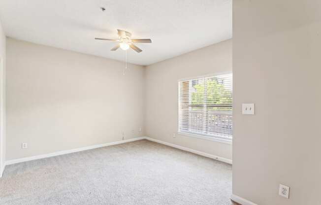 an empty living room with a large window and a ceiling fan