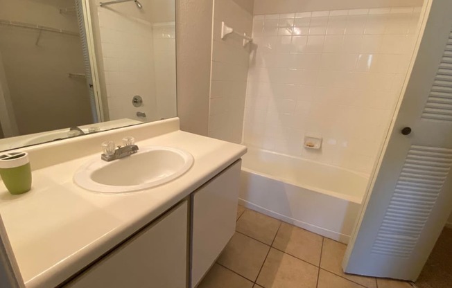 Bathroom with tile floors, toilet, shower tub combo with tile back splash, towel bar, white cabinets and view of closet