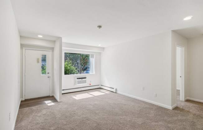 a view of living room with white walls and a window, front door and bedroom entrance