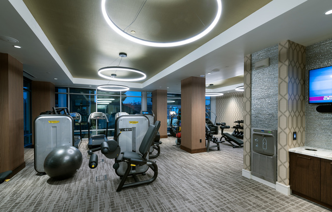 Alternate view of the indoor gym showing weight machines, treadmills, a wall-mounted HDTV, and a water station.