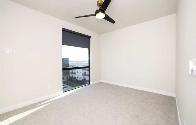 A room with a ceiling fan and a window overlooking a building.