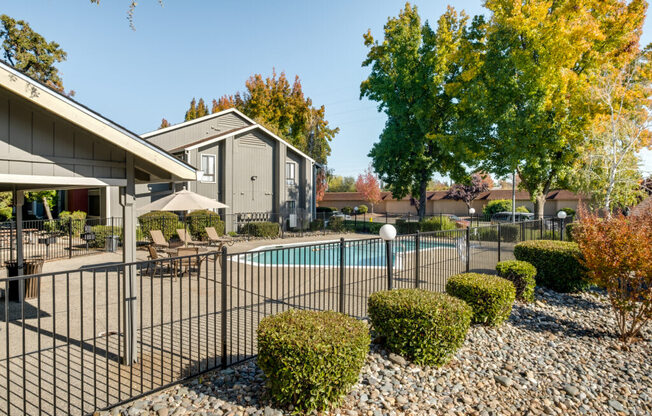 A pool surrounded by a black fence and bushes in front of a house.