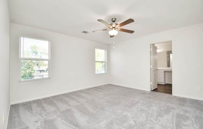 A room with a ceiling fan and two windows.