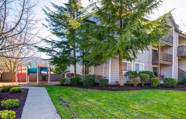 a sidewalk in front of an apartment building with a yard and trees