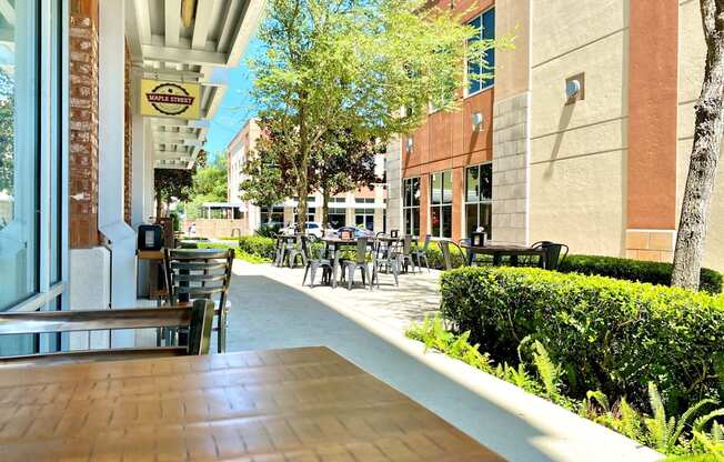 An outdoor dining area with chairs and tables in front of a local business near trees and bushes at the Tioga Town Center.