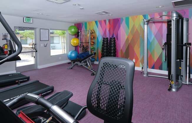 Cardio machines, cable machines, and body weight equipment in Fusion Las Vegas gym with pink flooring and colorful geometric wall.