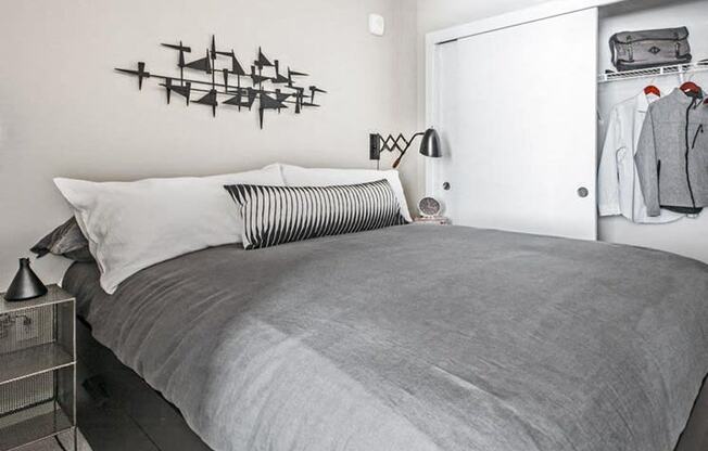 One-Bedroom Modern Apartments in Seattle, WA - Origin - Bedroom with Bed, Nightstand with Lamp, Wall Art, Spacious Closet, and Grey Carpet