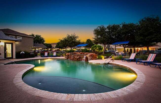 A pool surrounded by a brick patio at dusk.