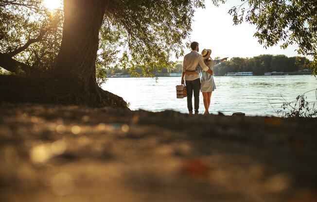 a man and a woman standing under a tree by the water at District at Riverside Apartments, Chattanooga