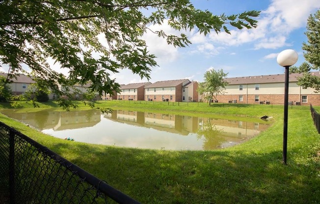 Pond in the middle of a grassy area with apartment buildings in the background at Maple Tree Apartments in LaPorte, IN