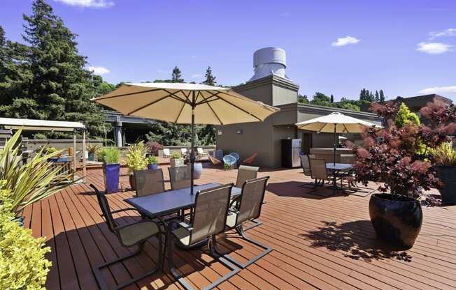 a large wooden deck with tables and chairs for lounging and potted flowers at Illumina Apartment Homes, Washington, 98102