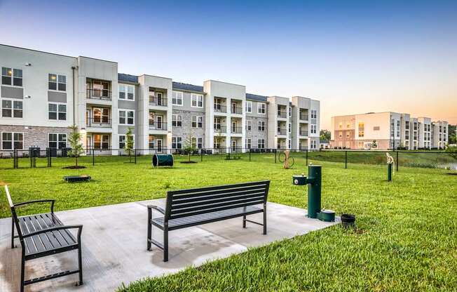 A park with benches and grass in front of apartment buildings.