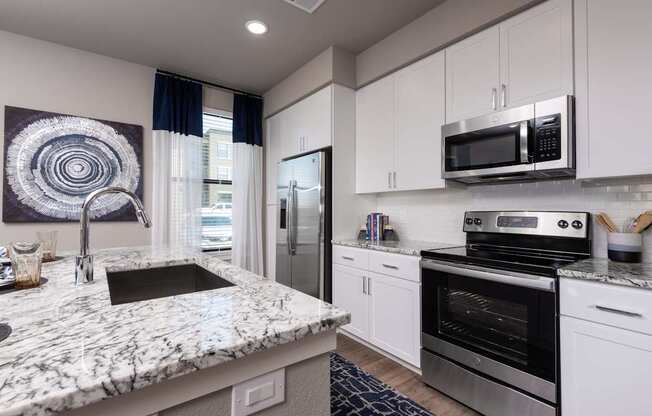 A modern kitchen with a marble countertop and stainless steel appliances.