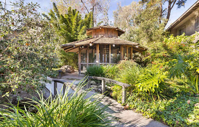A wooden bird aviary surrounded by green plants.