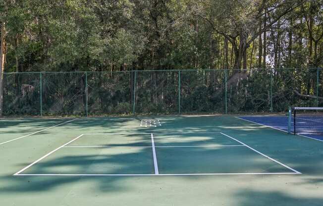 A tennis court surrounded by a fence and trees.