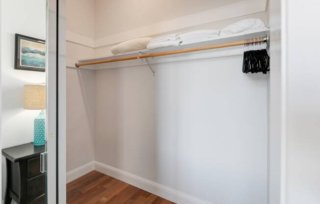 a closet with a white wall and a shelf with clothes on it and a mirror