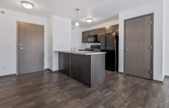 A kitchen with a black refrigerator and wooden floors.