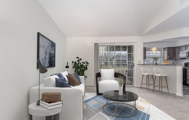 a living room with white furniture and a kitchen in the background