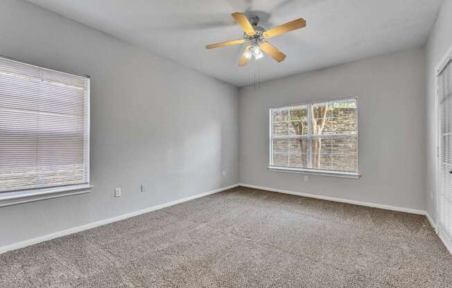 an empty living room with a ceiling fan and two windows