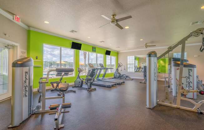 a gym with exercise machines and windows and a ceiling fan