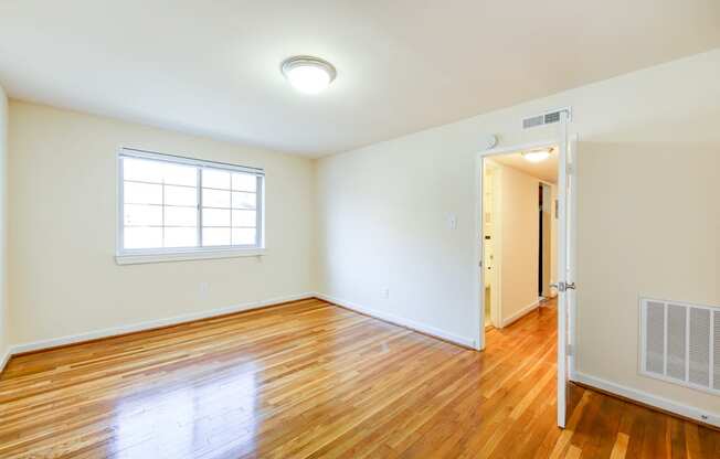 vacant living area with large windows, hard wood flooring and view of hallway in cambridge square apartments in bethesda md