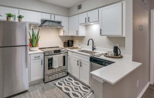 Modern L-shaped kitchen featuring breakfast bar, stainless dishwasher, and matte-black faucet.