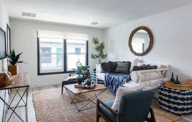 A living room with a white couch, a blue chair, and a round mirror on the wall.