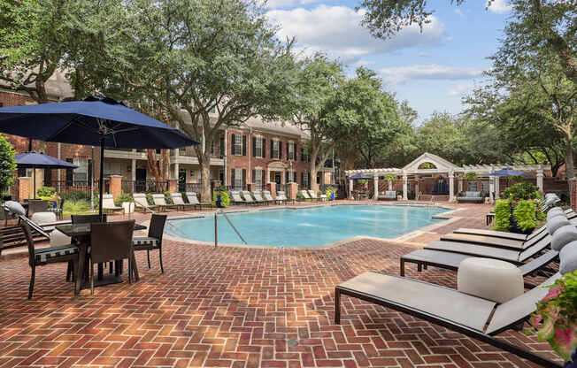 A pool surrounded by a brick patio and lounge chairs.