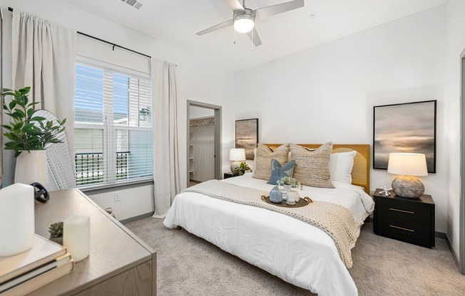 A bedroom with a large bed, a ceiling fan, and a window with blinds.