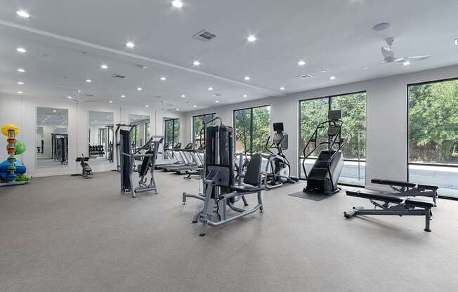 A spacious gym with a variety of equipment and a view of trees outside the windows.