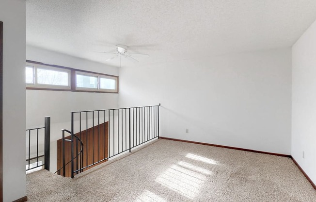 an empty living room with a balcony and a ceiling fan