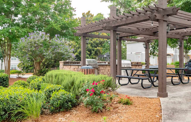 A wooden pergola with a sign on it is surrounded by greenery and a picnic table.