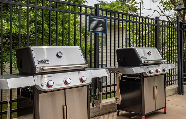 Two grills are placed next to a fence.