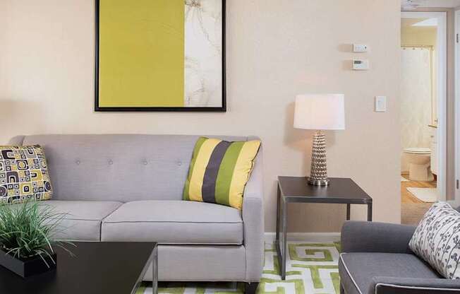 A living room with a grey couch, a black coffee table, and a green rug.
