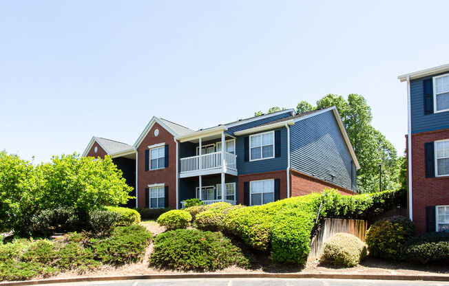 a brick apartment building with a blue roof and green shrubbery in front of it