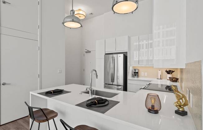 a kitchen with white cabinetry and a large white island with a sink and two stools