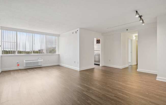 the living room and dining room of an apartment with wood flooring and a window