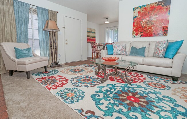 Large model living room with a white couch and a large floral rug at Laurel Parc apartments in Shreveport, LA.