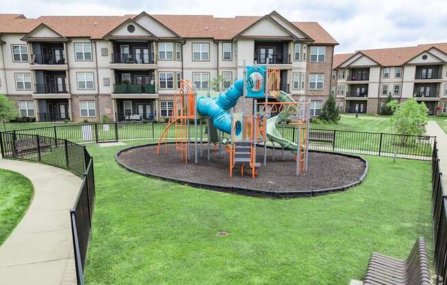 A playground with a slide and a green lawn in front of apartment buildings.