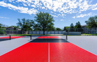 a tennis court with red and black turf and a tree