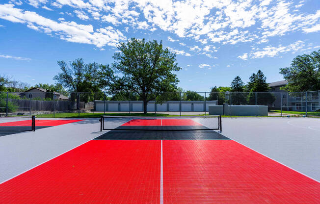 a tennis court with red and black turf and a tree