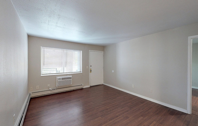 Bright and inviting living room with sleek wood flooring, large window, and modern air conditioning unit.