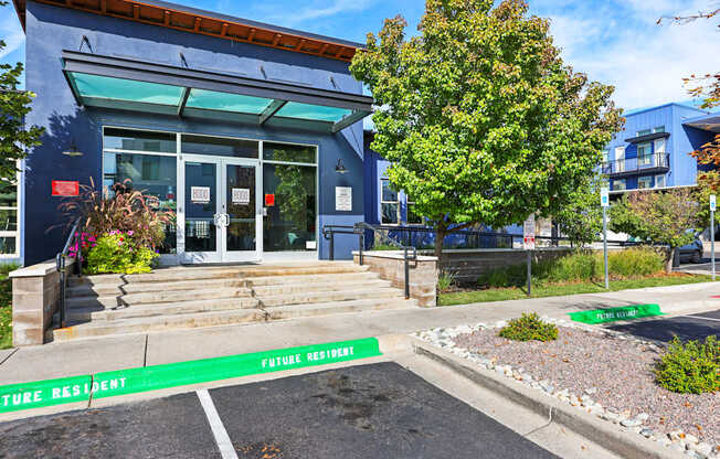 A blue building with a glass door and windows, with a green sign in front that says "FUTURE RESIDENT".