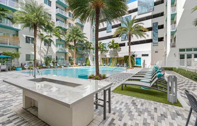 a swimming pool with a table and chairs in front of an apartment building