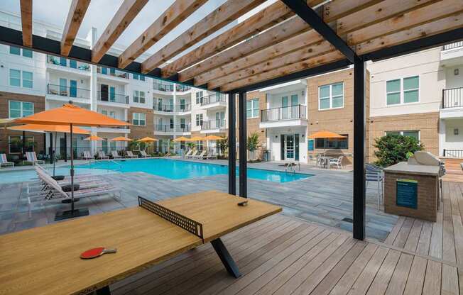 A red paddle is on a wooden table in the foreground of a pool area.