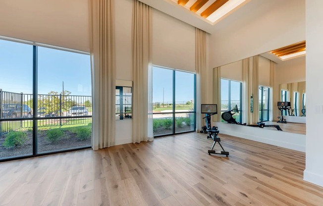 A spacious room with wooden floors and large windows overlooking a garden.