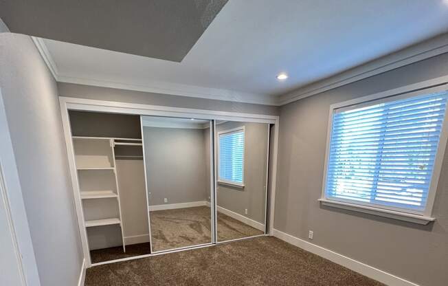 View of bedroom with carpet flooring, sliding mirror closet door with built in shelving, and well lit window